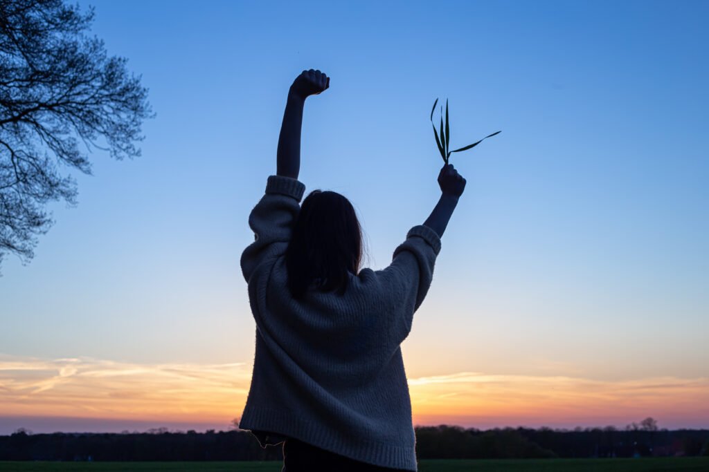 Silhouette of a woman at sunset in a field against the sky, rear view, the concept of freedom and love for nature.